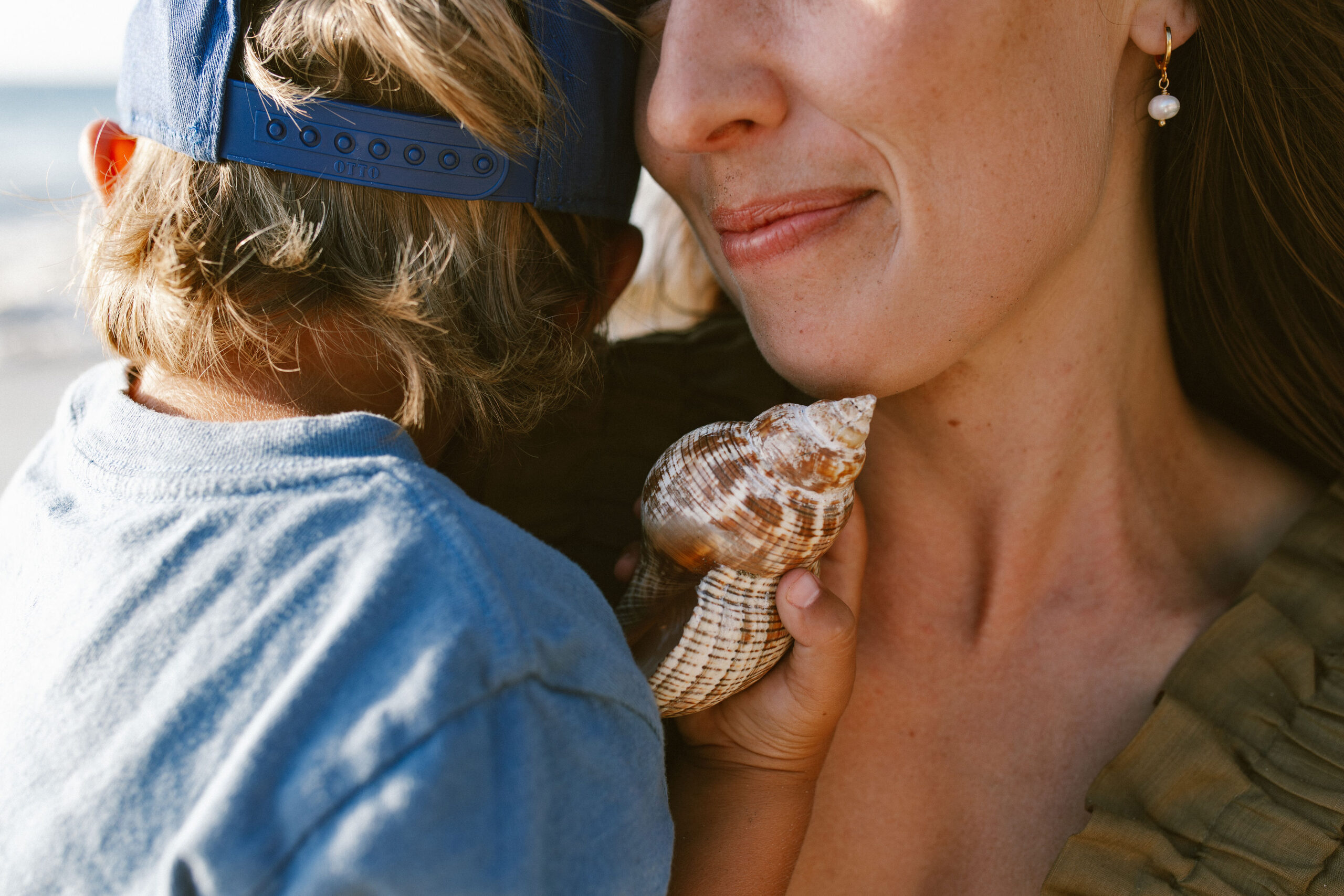 A child holding a spiral seashell up against his mother's shoulder